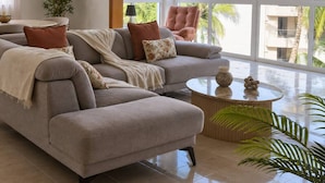 Una sala de estar moderna con un sofá modular, una mesa de centro redonda y vistas a palmeras a través de amplios ventanales.