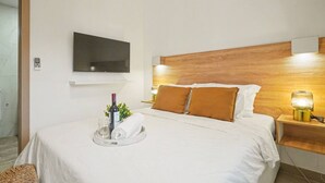 A hotel room with a bed, a television mounted on the wall, a bedside table with a lamp, and a tray with a bottle and glasses. - Modern 2BR Pool 5 Min to Coco Bongo Downtown (Punta Cana)