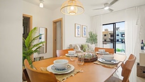 Área de refeições com mesa posta para quatro pessoas, ventilador de teto e vista para o exterior.