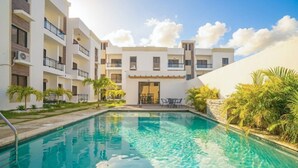 A hotel with a swimming pool, multiple balconies, and a clear sky. - Modern 2BR Pool 5 Min to Coco Bongo Downtown (Punta Cana)