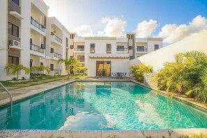 A hotel with a swimming pool, multiple balconies, and a clear sky. - Modern 2BR Pool 5 Min to Coco Bongo Downtown (Punta Cana)