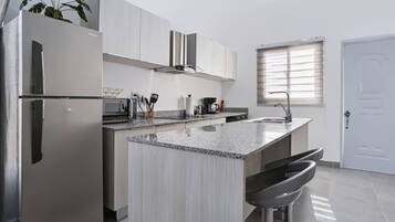 Una cocina moderna con electrodomésticos de acero inoxidable, encimera de granito y una ventana con persianas.