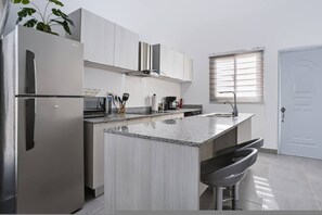 A modern kitchen with stainless steel appliances, a granite countertop, and a window with blinds.