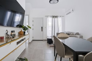 A modern living room with a flat-screen TV, a dining area with a table and chairs, and a kitchen area with a stove and cabinets. - Spacious 3BR Home Pool Macao Beach (Punta Cana)