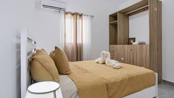 Un dormitorio con cama, mesita de noche, aire acondicionado, armario y ventana con cortinas.