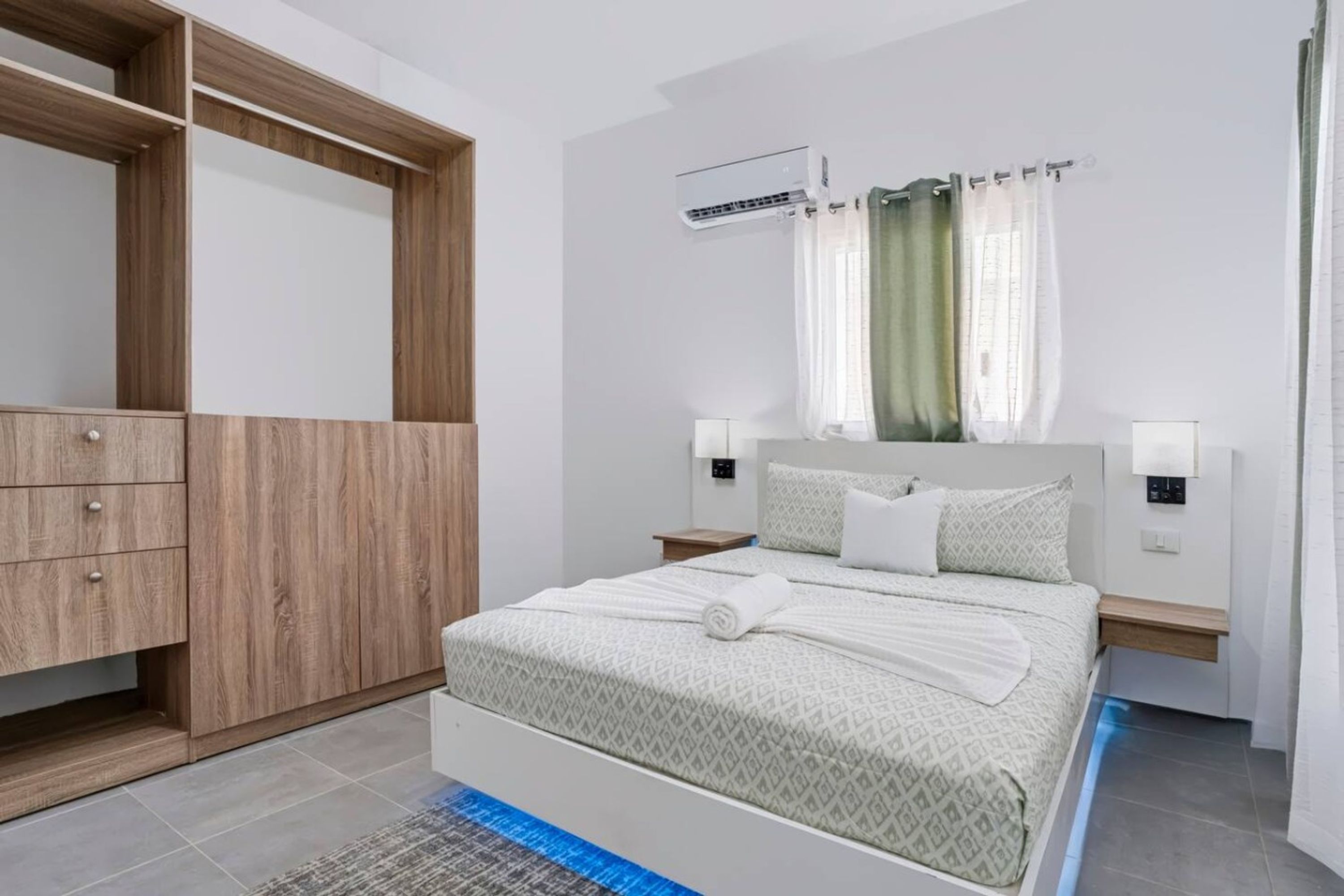 Un dormitorio moderno con cama, armario, mesita de noche y aire acondicionado.
