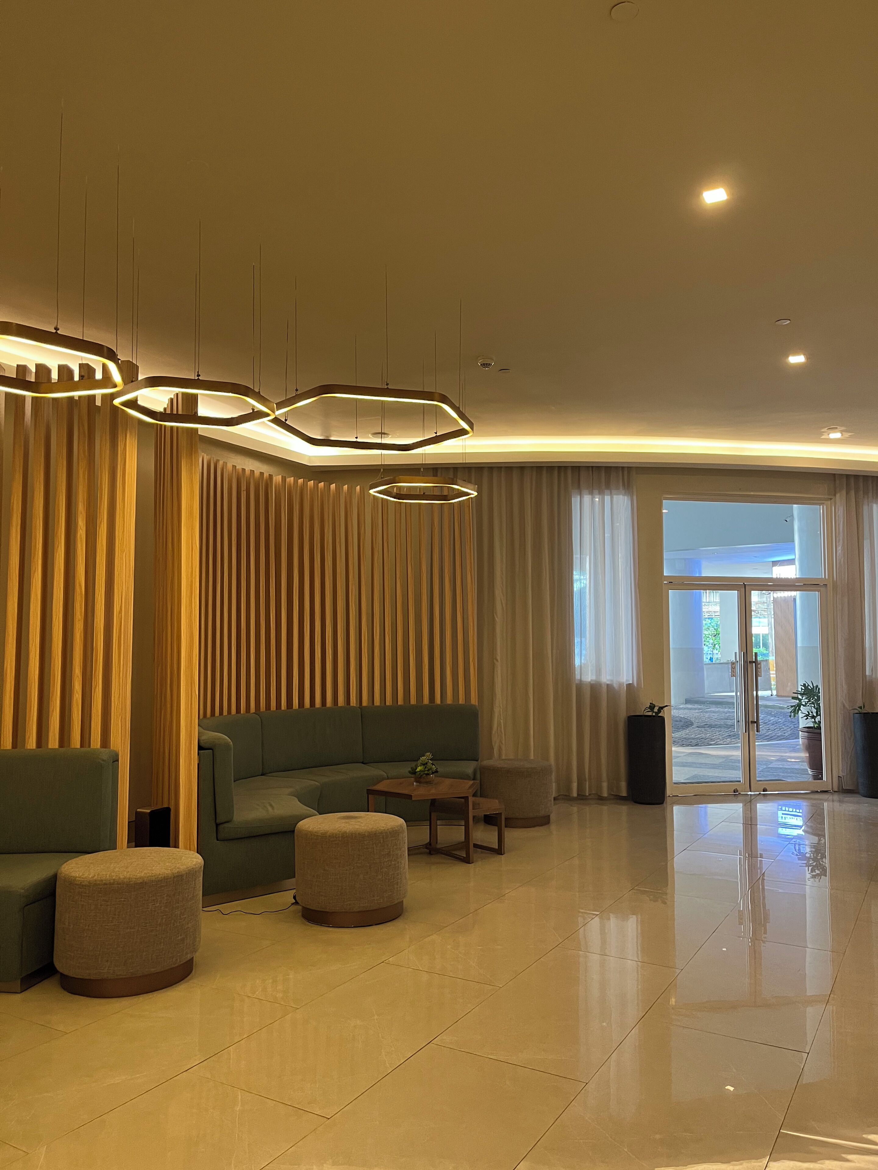 Eine moderne Lobby mit einem Ecksofa, runden Hocker, einer Holzvertäfelung und einem Glastür-Eingang.