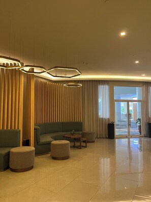 A modern lobby with a sectional sofa, round ottomans, a wooden accent wall, and a glass door entrance.