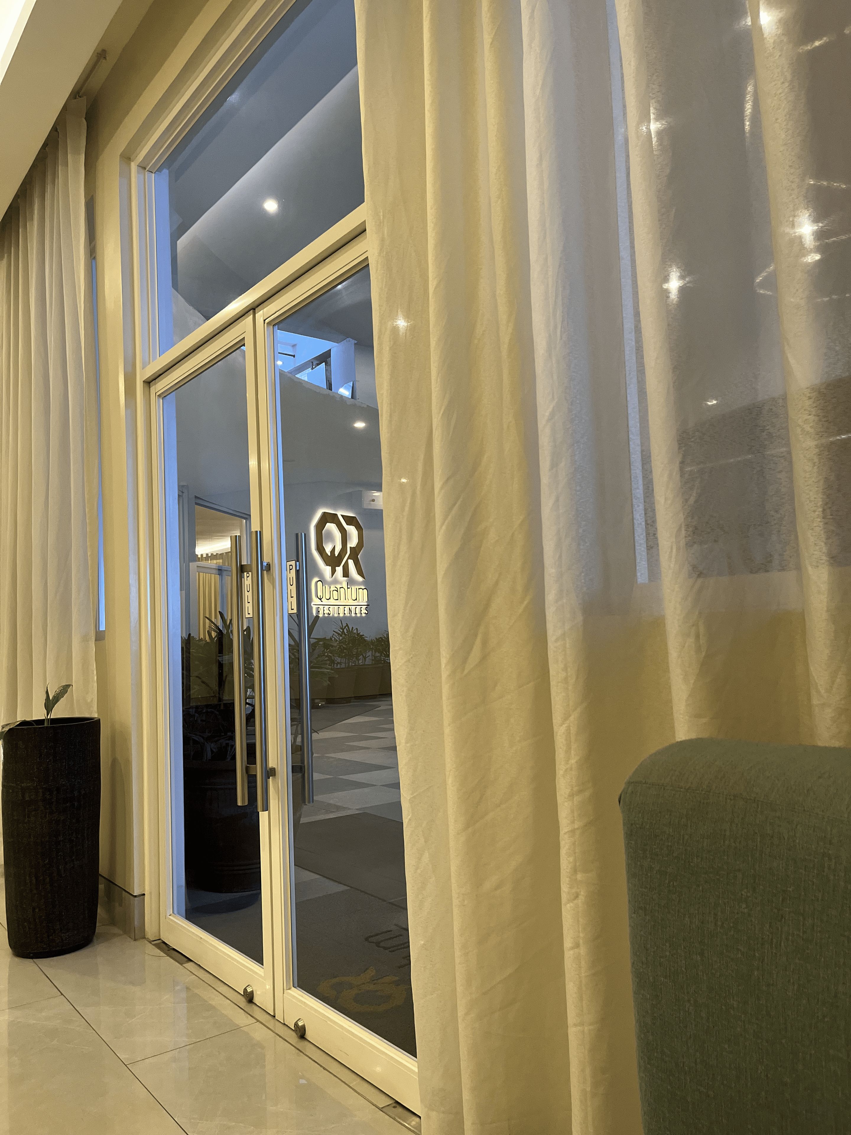 A hotel entrance with a glass door, a sign for Quantum Residences, and a potted plant.