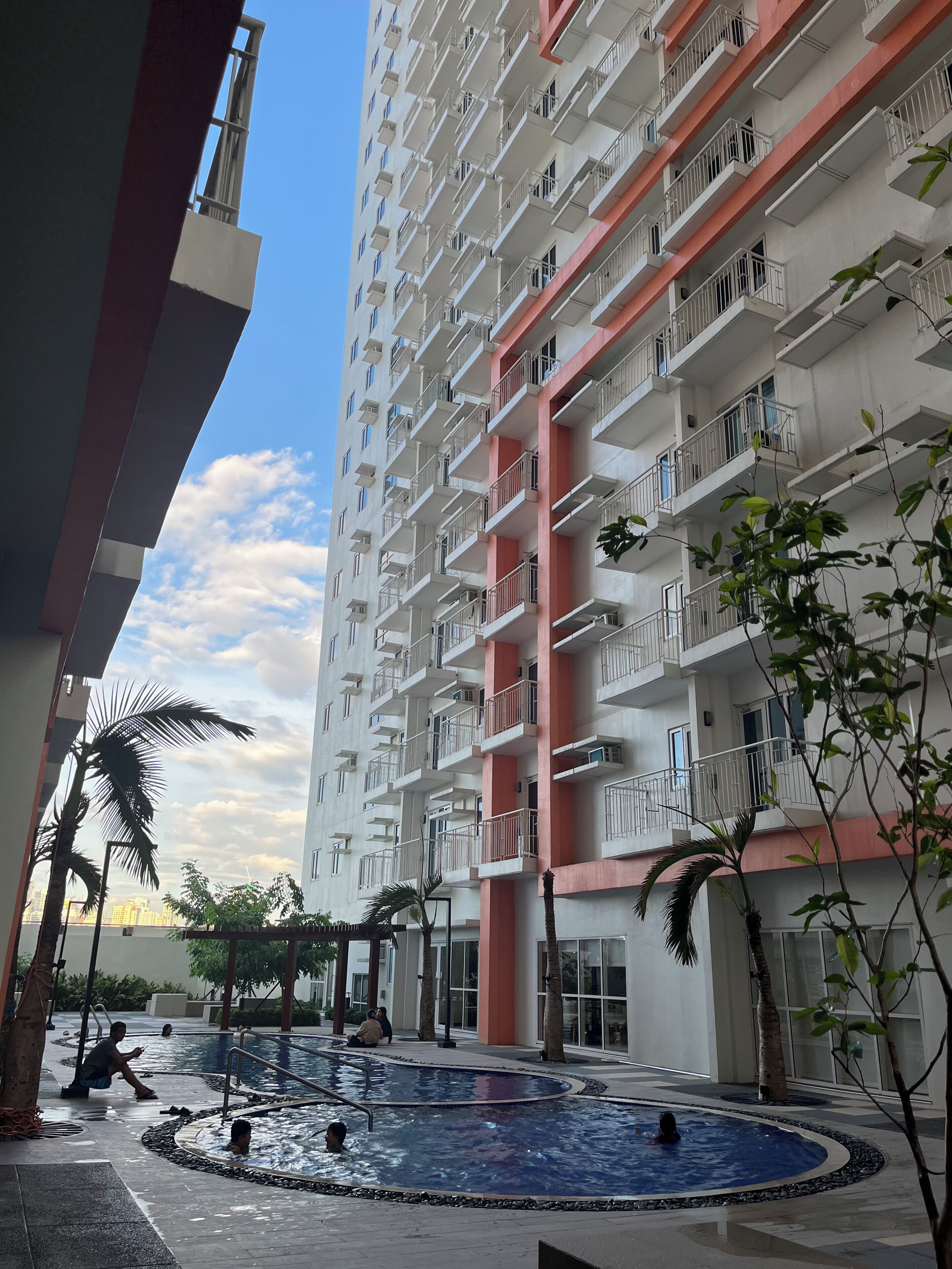 Un immeuble résidentiel doté de nombreux balcons, d’un espace piscine et entouré de verdure.
