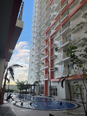 Edificio residenziale con numerosi balconi, area piscina e vegetazione circostante.