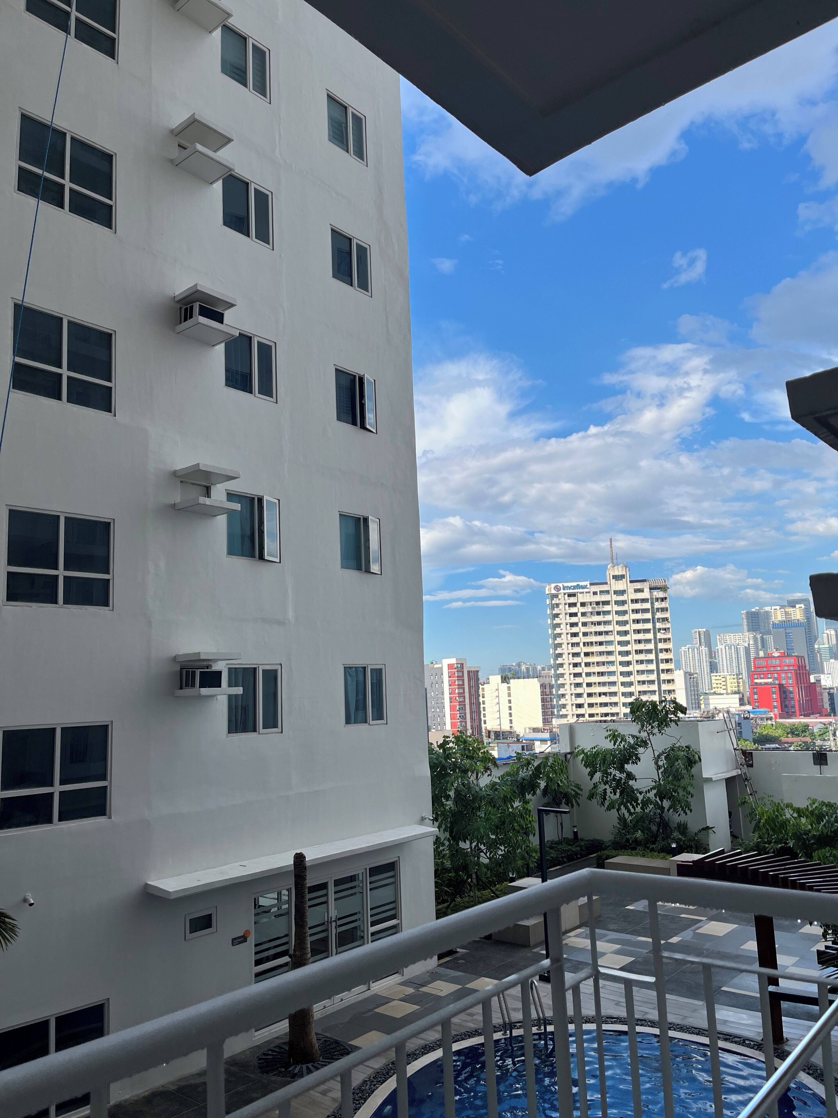 Un edificio moderno con múltiples ventanales y unidades de aire acondicionado, un área de piscina con solárium y vistas a un paisaje urbano.