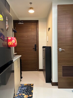 A modern kitchen with a built-in refrigerator, a microwave, and a coffee machine. There is a wooden door with a handle and a small window.