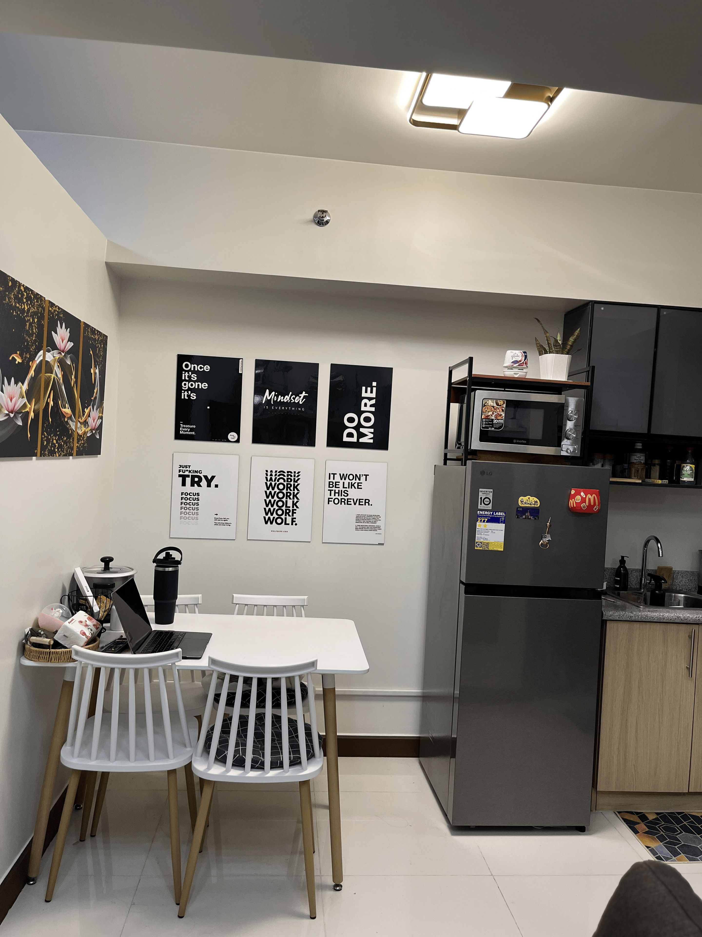 Una cocina moderna con una mesa blanca, dos sillas, un microondas y un refrigerador.