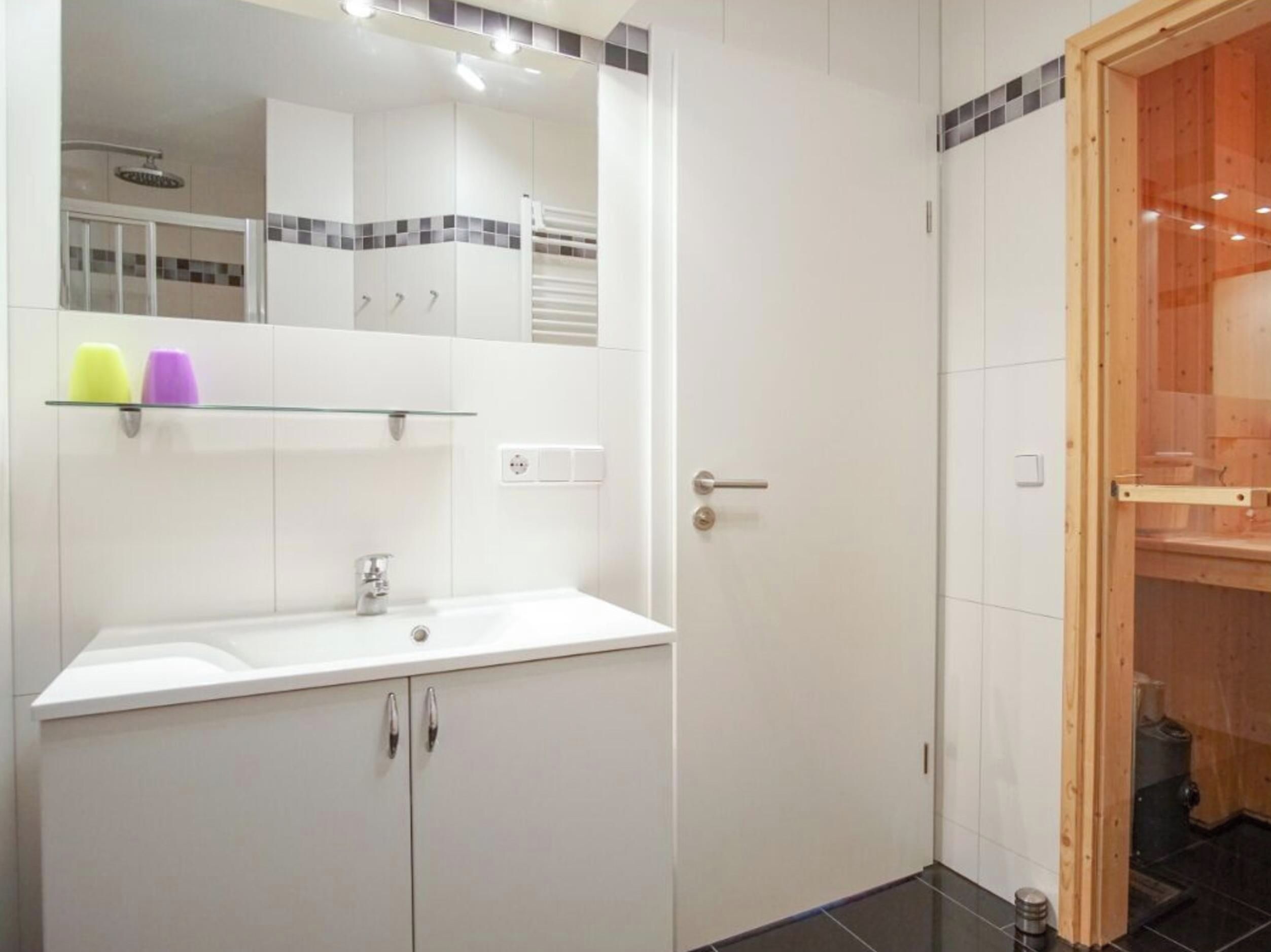 A bathroom with a white sink, mirror, and cabinets. There is a shower area visible in the background.