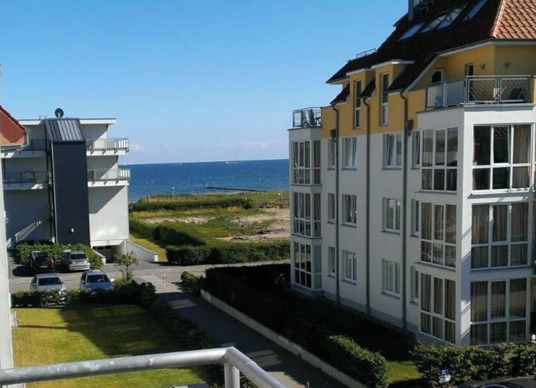 A residential building with a view of the sea, a parking area, and a pathway leading to the entrance.
