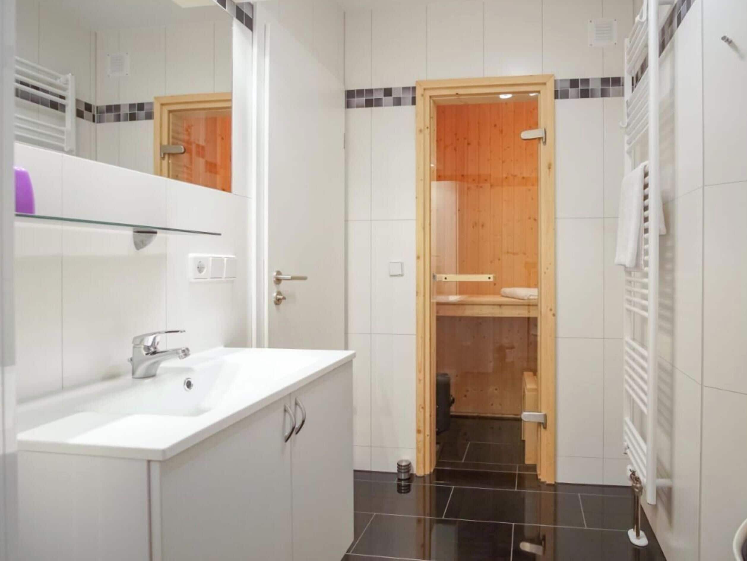 A modern bathroom with a white sink, a mirror, and a wooden door leading to a shower area.