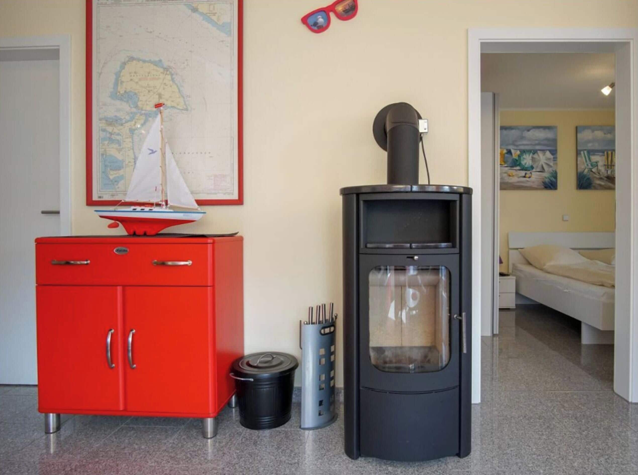 Una habitación con un armario rojo, un mapa en la pared, una estufa y una cama con un cuadro.