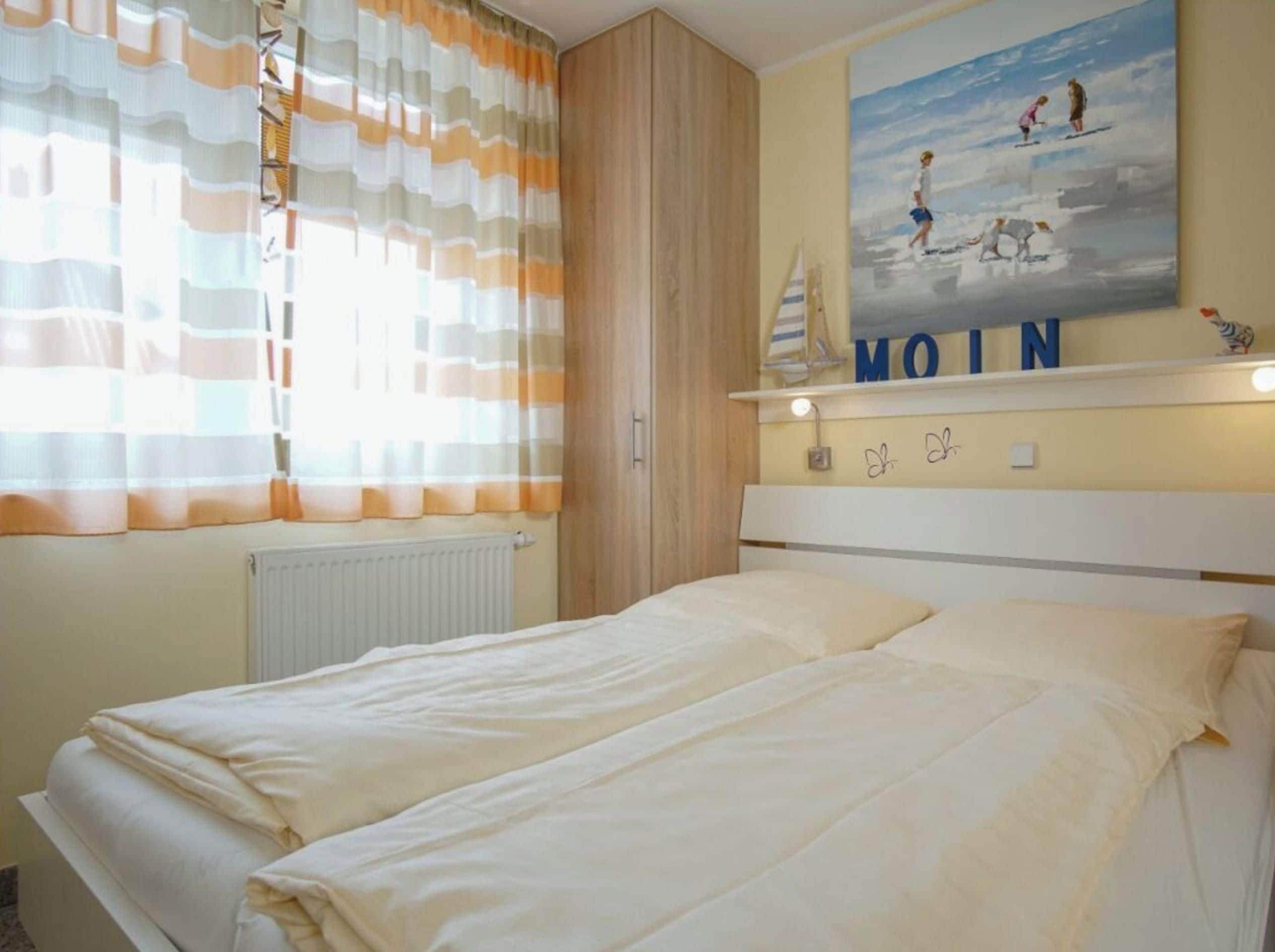 A bedroom with a bed, curtains, a painting, and a shelf with a sailboat and the word 'MOIN'.