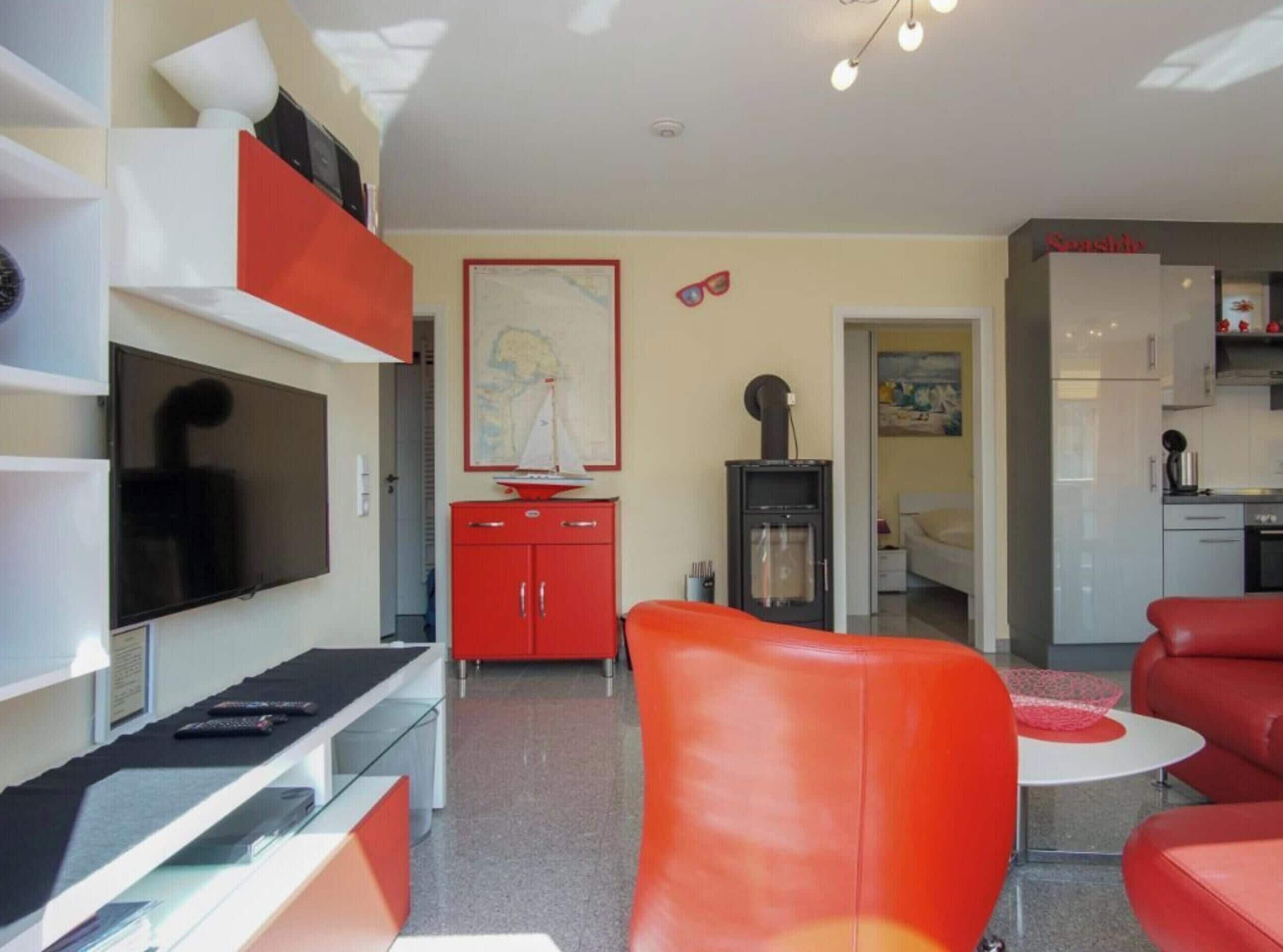 A modern living room with a flat-screen TV, red furniture, a map on the wall, and a kitchen area.