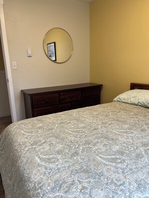 A bedroom with a bed, dresser, and a round mirror on the wall. - Sequim and Sun and Fun (Sequim)
