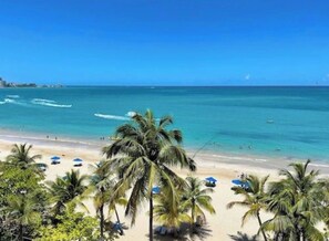 Ein Strand mit Palmen, klarem, blauem Wasser und Sonnenschirmen.