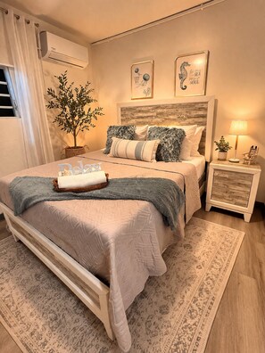 Ein Schlafzimmer mit einem Bett, einem Nachttisch, einer Lampe, einer Zimmerpflanze und Wandbildern.