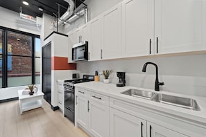 A modern kitchen with white cabinets, a stainless steel sink, a black faucet, and a built-in microwave. - Dine, Shop & Explore | Walk to Petco Park & More!! (San Diego)