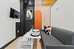 A modern living space with a dining area, a grey sofa, and a TV mounted on the wall. - Dine, Shop & Explore | Walk to Petco Park & More!! (San Diego)