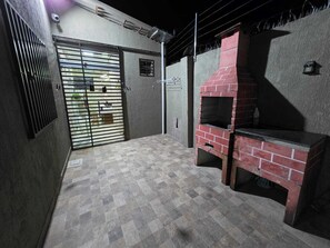 Ein Zimmer mit Fliesenboden, einem Backofen aus Ziegeln, einem Metallgitter und einer Wandleuchte.