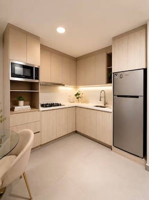 Une cuisine moderne avec des meubles de couleur bois clair, un réfrigérateur en acier inoxydable, un four à micro-ondes et une table en verre.
