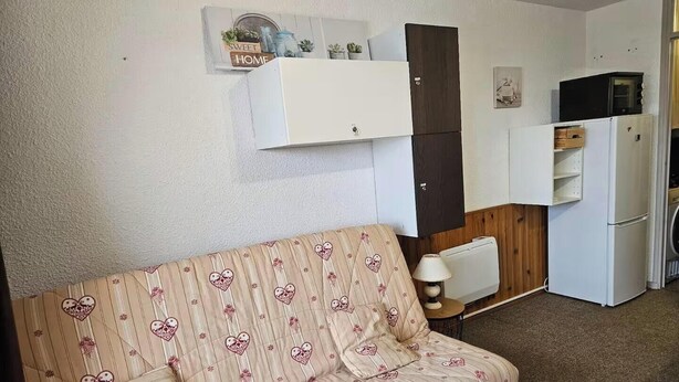 Un espai habitable compacte amb sofà, petita cuina i zona de dinar.