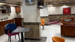 Um saguão de hotel com um pilar de mármore, área de estar e uma kitchenette ao fundo.