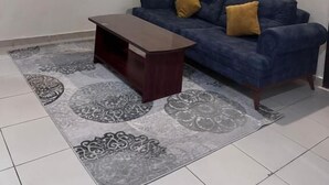 Uma sala de estar com um sofá azul, uma mesa de centro de madeira, tapete estampado e um aparelho de ar condicionado na parede.