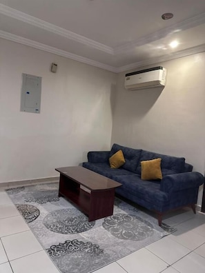 A living room with a blue sofa, a wooden coffee table, patterned rug, and an air conditioning unit on the wall. - Jumeirah Line Serviced Apartments (Jeddah)