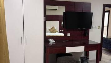 A hotel room with a desk, a television, a wardrobe, and a small seating area.