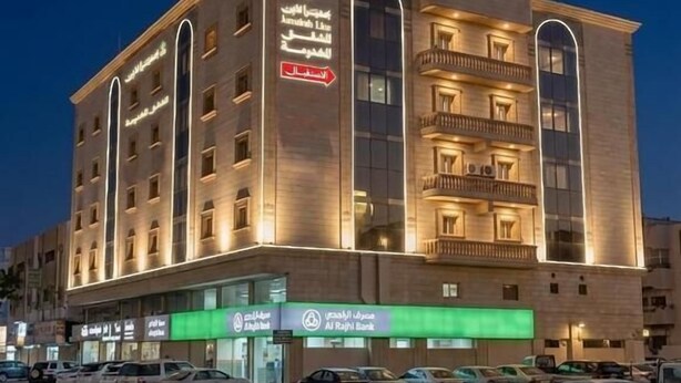Um hotel com vários andares, entrada destacada e placa verde indicando agência bancária.