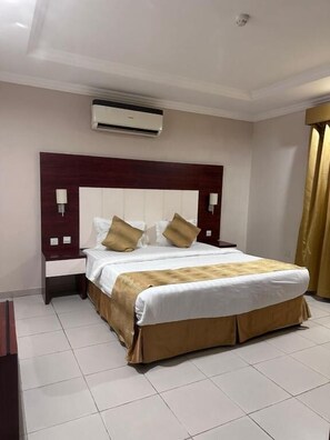 Habitación de hotel con una cama grande, cabecera, dos mesitas de noche, unidad de aire acondicionado y cortina.