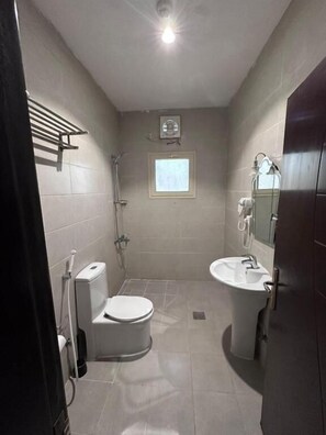 A bathroom with a toilet, sink, shower, and a window. - Jumeirah Line Serviced Apartments (Jeddah)