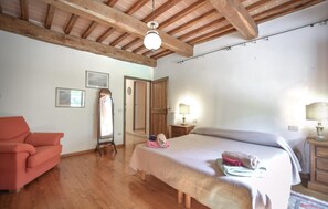 Un dormitorio con cama, una silla, un espejo y vigas de madera en el techo.