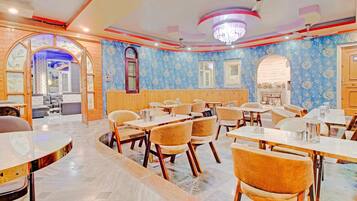 A restaurant with multiple tables and chairs, a chandelier, and patterned wallpaper.