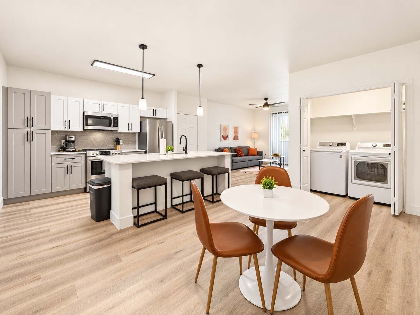 Een moderne keuken met witte kasten, een centraal eiland, barkrukken en een eettafel met stoelen.