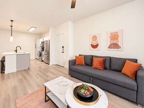 A modern living space with a grey sofa, a marble coffee table, and a kitchen area with white cabinetry and stainless steel appliances. - CozySuites Glendale - Westgate w pool! 2BR 2BA (Glendale)