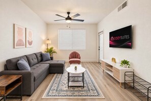 A modern living room with a sectional sofa, a single chair, a coffee table, a TV, and a ceiling fan. - CozySuites Glendale - Westgate w pool! 1BR 1BA (Glendale)