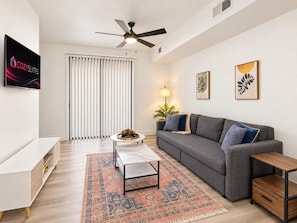 Ein modernes Wohnzimmer mit einem grauen Sofa, einem Couchtisch, einem Fernseher und einem Deckenventilator.