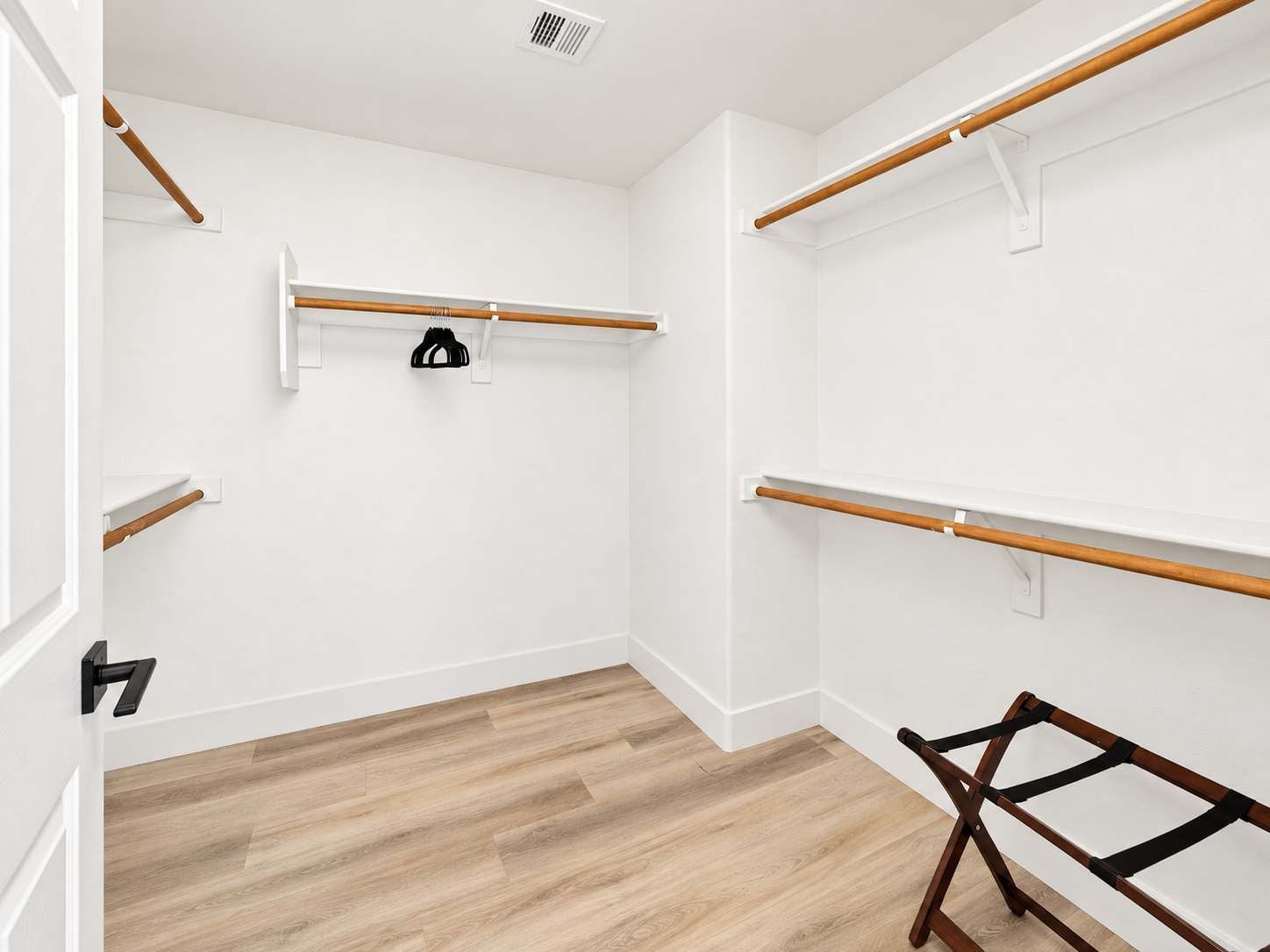 Ein Zimmer mit weißen Wänden, Holzboden und einem Holzstuhl. Zwei weiße Regale und eine schwarze Tasche hängen an einem der Regale.