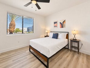 A modern bedroom with a bed, two bedside tables with lamps, a ceiling fan, a window with blinds, and artwork on the wall. - CozySuites Glendale - Westgate w pool! 1BR 1BA (Glendale)