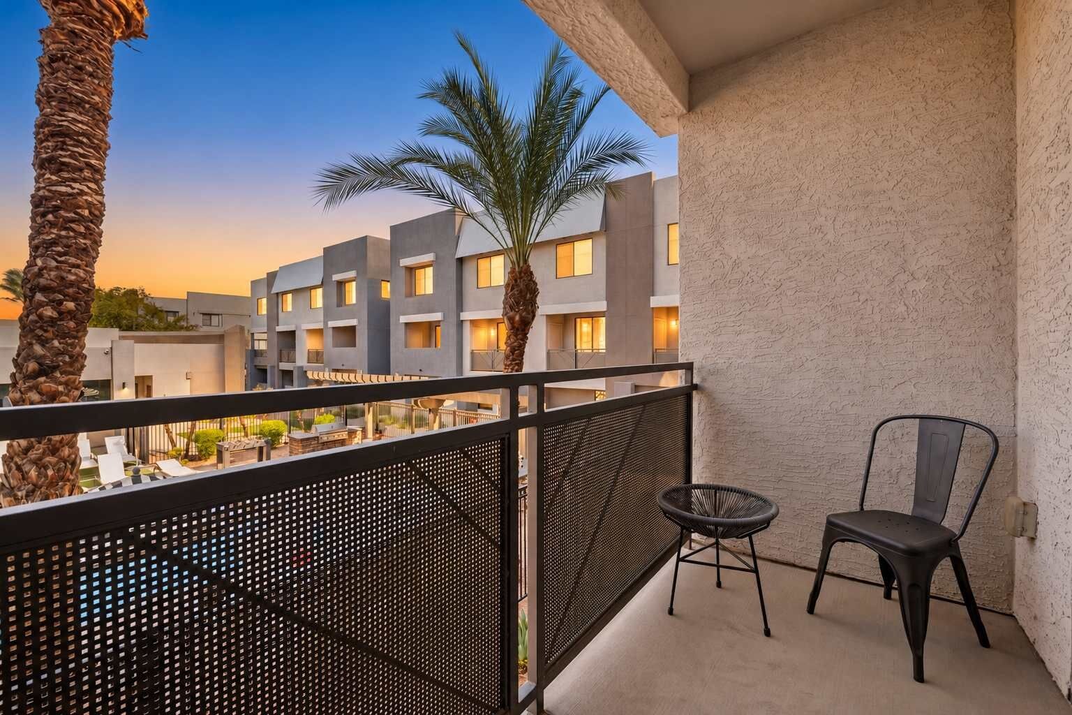 A balcony with a metal railing, a chair, and a palm tree.