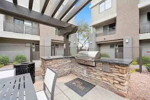 An outdoor patio with a grill and seating area, surrounded by stone walls and a metal fence. - CozySuites Glendale - Westgate w pool! 1BR 1BA (Glendale)