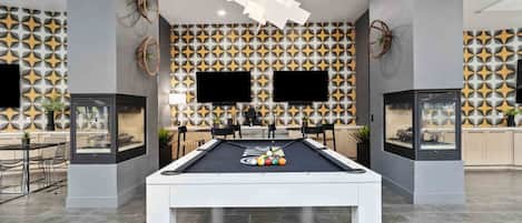 Ein moderner Indoor-Billiardtisch mit geometrisch gemusterten Wänden im Hintergrund, ein flachbildfernseher darüber angebracht und ein schlichtes Decken-Design.